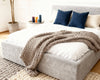 #Close-up of O2 Soft Frame Bed in Platinum Grey with a chunky knit throw, navy and beige throw pillows, and minimalist decor