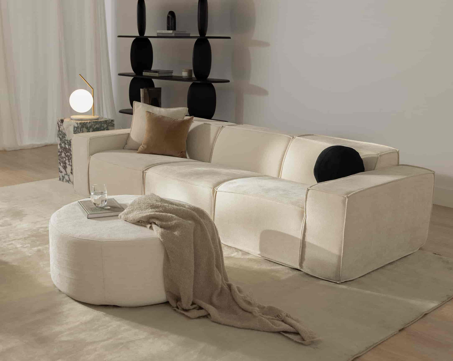 #Modular beige sofa from Rove Lab in a modern living room, featuring a marble side table with a spherical lamp, minimalistic shelving, and soft fabric decor on a round ottoman